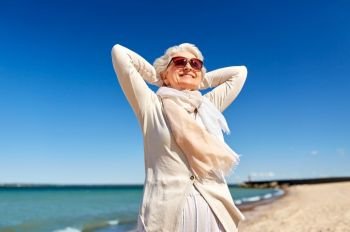 people and leisure concept - portrait of happy senior woman in sunglasses and scarf on beach in estonia. portrait of senior woman in sunglasses on beach