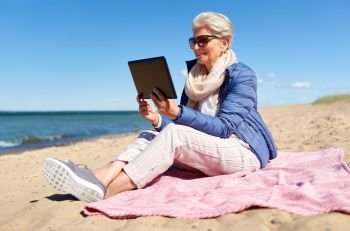 technology, old people and leisure concept - senior woman with tablet computer on beach in estonia. senior woman with tablet computer on beach