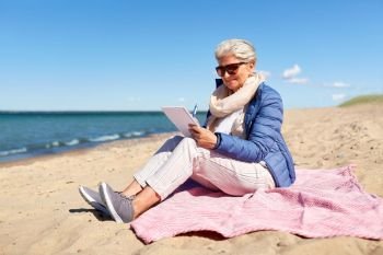 people and leisure concept - happy senior woman writing to notebook on summer beach in estonia. senior woman writing to notebook on summer beach