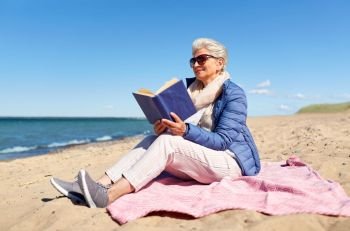 people and leisure concept - happy senior woman reading book on summer beach in estonia. happy senior woman reading book on summer beach