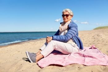 people and leisure concept - happy senior woman in sunglasses and jacket on beach in estonia. happy senior woman in jacket on beach