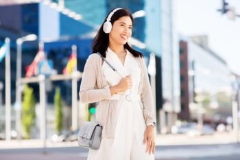 technology, leisure and people concept - happy smiling asian woman with headphones listening to music in city. happy smiling asian woman with headphones in city