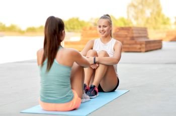 fitness, sport and healthy lifestyle concept - smiling young women or female friends sitting on exercise mats outdoors. happy women sitting on exercise mats outdoors