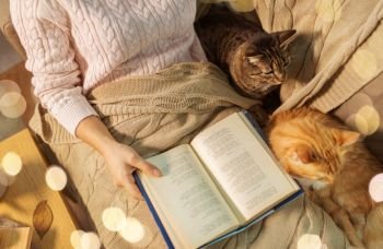 hygge, literature and people concept - close up of red and tabby cat and female owner reading book in bed at home. red and tabby and owner reading book at home