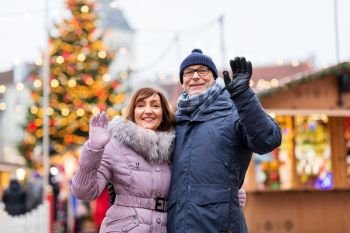 winter holidays and people concept - happy senior couple waving hands at christmas market on town hall square in tallinn, estonia. senior couple waving hands at christmas market