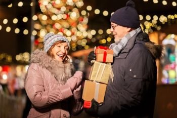 love, winter holidays and people concept - happy senior couple with gift at christmas market on town hall square in tallinn, estonia. happy senior couple with gift at christmas market