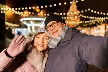 winter holidays and people concept - happy senior couple taking selfie at christmas market on town hall square in tallinn, estonia. senior couple taking selfie at christmas market