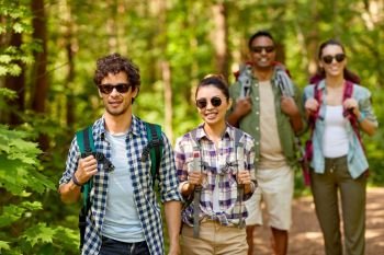 travel, tourism, hike and people concept - group of friends walking with backpacks in forest. group of friends with backpacks hiking in forest