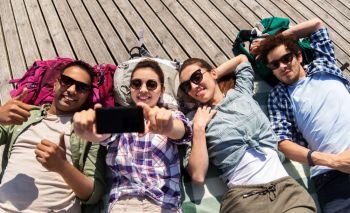 travel, tourism and people concept - group of friends or tourists with backpacks lying on wooden terrace and taking selfie by smartphone. friends or tourists with backpacks taking selfie