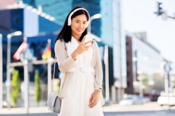 technology, leisure and people concept - happy smiling asian woman with smartphone and headphones listening to music in city. asian woman with smartphone and headphones in city