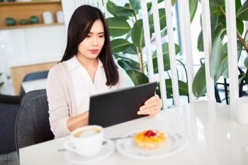 technology and people concept - asian woman with tablet pc computer and cake at cafe or coffee shop. asian woman with tablet pc at cafe or coffee shop