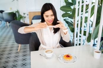 technology, leisure and people concept - happy asian woman with smartphone photographing her coffee and cake at cafe. woman photographing coffee by smartphone at cafe