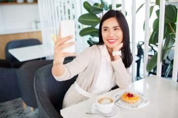 technology and people concept - happy asian woman with cake and coffee taking selfie by smartphone at cafe. asian woman taking selfie by smartphone at cafe
