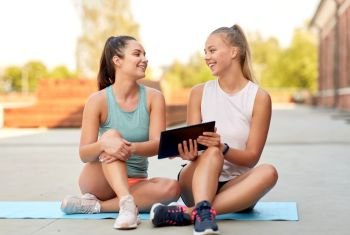 fitness, sport and healthy lifestyle concept - smiling young women or female friends with tablet computer on rooftop. sporty women or friends with tablet pc on rooftop