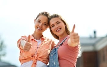 leisure and friendship concept - happy smiling teenage girls or best friends showing thumbs up outdoors in summer. teenage girls or best friend showing thumbs up
