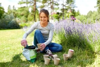 gardening and people concept - happy young woman or gardener filling pots with soil at summer garden. woman filling pots with soil at summer garden