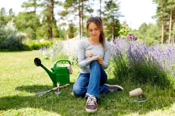 gardening and people concept - young woman or gardener writing to notebook at summer garden. young woman writing to notebook at summer garden