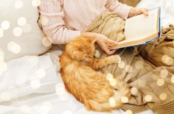 pets, hygge and people concept - red tabby cat and female owner reading book in bed at home. red cat and female owner reading book at home
