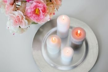 decoration, hygge and cosiness concept - candles burning on table and flowers at cozy home. candles burning on table and flowers at cozy home