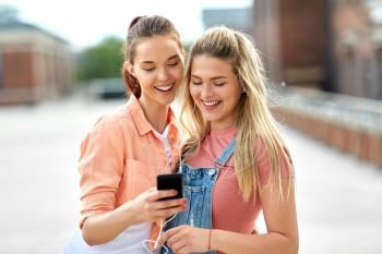 leisure and technology concept - smiling teenage girls or best friendswith earphones listening to music on smartphone on city roof top in summer. teenage girls listening to music on smartphone