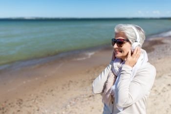 technology, old people and leisure concept - senior woman in headphones and sunglasses listening to music on summer beach in estonia. old woman in headphones listens to music on beach