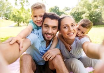 family, leisure and technology concept - happy mother, father and two little sons having picnic and taking selfie at summer park. family having picnic and taking selfie at park