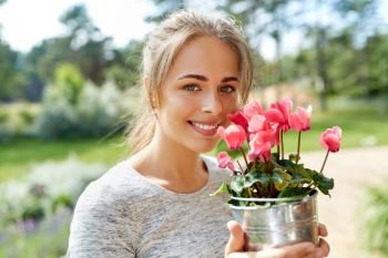 farming, gardening and people concept - happy young woman with pink cyclamen flowers in pot at summer garden. young woman with cyclamen flowers at summer garden