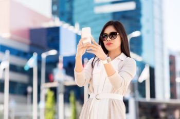 communication, lifestyle and technology concept - young asian woman taking selfie by smartphone on city street. asian woman taking selfie by smartphone in city