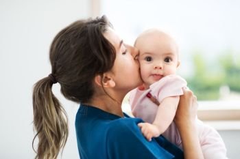 babyhood, motherhood and people concept - mother holding and kissing baby daughter at home. mother holding and kissing baby daughter at home