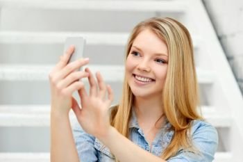 technology and people concept - smiling teenage girl taking selfie by smartphone on stairs. teenage girl taking selfie by smartphone on stairs