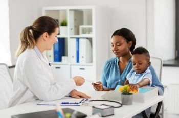 medicine, healthcare and pediatry concept - caucasian doctor giving prescription to african american mother with baby son at clinic. happy mother with baby son and doctor at clinic