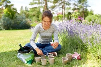 gardening and people concept - happy young woman planting seeds to pots at summer garden. woman planting seeds to pots at summer garden