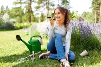 gardening, technology and people concept - happy young woman or gardener with garden tools calling on smartphone or using voice command recorder. gardener recording voice message by smartphone