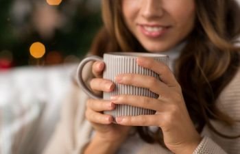 christmas, winter holidays and hygge concept - close up of happy woman with cup of coffee or tea at home. close up of woman with cup of coffee on christmas