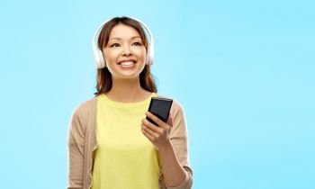 people, technology and audio equipment concept - happy asian young woman in headphones listening to music on smartphone over blue background. asian woman in headphones listening to music