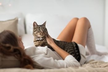 pets, comfort, rest and people concept - happy young woman with cat lying in bed at home. happy young woman with cat lying in bed at home