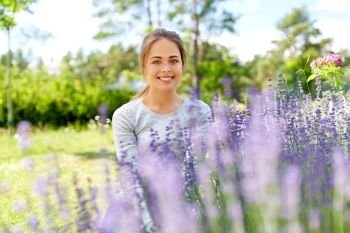 gardening and people concept - happy young woman sitting near lavender flowers on summer garden bed. young woman and lavender flowers at summer garden