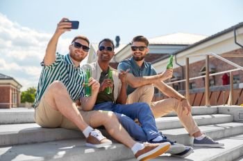 leisure, technology and people concept - happy male friends taking selfie by smartphone and drinking beer on street in summer. men drinking beer and taking selfie by smartphone