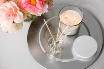 decoration, hygge and cosiness concept - aroma reed diffuser, burning candle and flower bunch on wooden table. aroma reed diffuser, candle and flowers on table