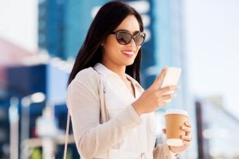communication, lifestyle and technology concept - happy smiling young asian woman in sunglasses with takeaway coffee cup and smartphone on city street. smiling woman with smartphone and coffee in city