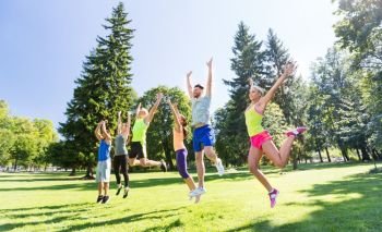 fitness, sport and healthy lifestyle concept - group of happy people jumping high at park in summer. group of happy friends jumping high at park