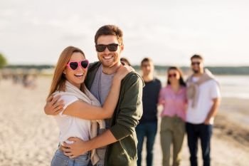 valentine’s day, relationships and people concept - happy couple with group of friends hugging on beach in summer. happy friends walking along summer beach