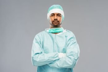 medicine, surgery and people concept - indian male doctor or surgeon in protective wear over grey background. indian male doctor or surgeon in protective wear