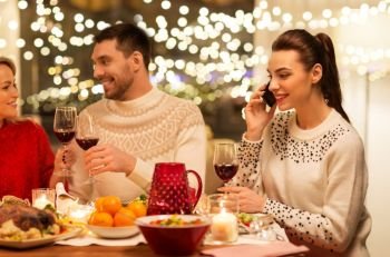 holidays and celebration concept - happy woman calling on smartphone while having christmas dinner with friends at home. happy friends having christmas dinner at home
