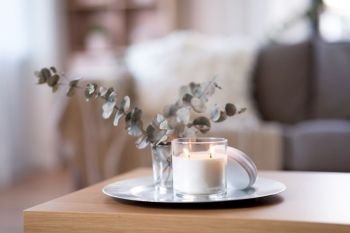 decoration, hygge and cosiness concept - burning white fragrance candle on tray and branches of eucalyptus populus on table at cozy home. burning fragrance candle on table at cozy home