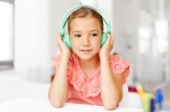 children and technology concept - happy girl in headphones listening to music at home desk. girl in headphones listening to music at home