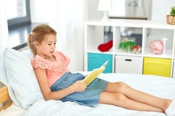 people, childhood and leisure concept - happy little girl reading book at home. happy little girl reading book at home
