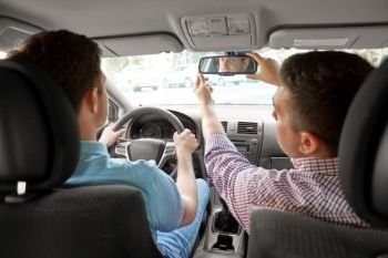 driver courses and people concept - man and driving school instructor adjusting rearview mirror in car. car driving school instructor teaching man driver