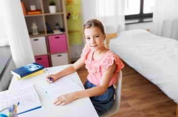 children, education and learning concept - student girl with book writing to notebook at home. student girl with book writing to notebook at home