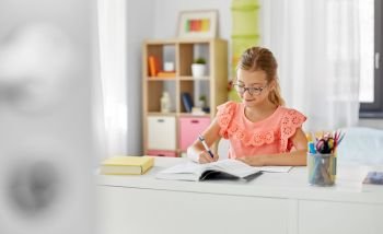 children, education and learning concept - student girl with book writing to notebook at home. student girl with book writing to notebook at home